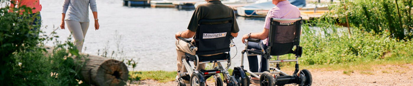 Layoutbild Seitenkopf zeigt zwei Personen in einem faltbaren Elektrorollstuhl an einem Seeufer